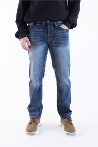 A person wearing medium-wash blue denim jeans with a dark ribbed sweater and brown shoes, standing against a plain white studio background.
