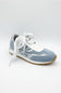 A light blue and white low-top sneaker with white laces and a gum-colored outsole, photographed on a light gray studio background.