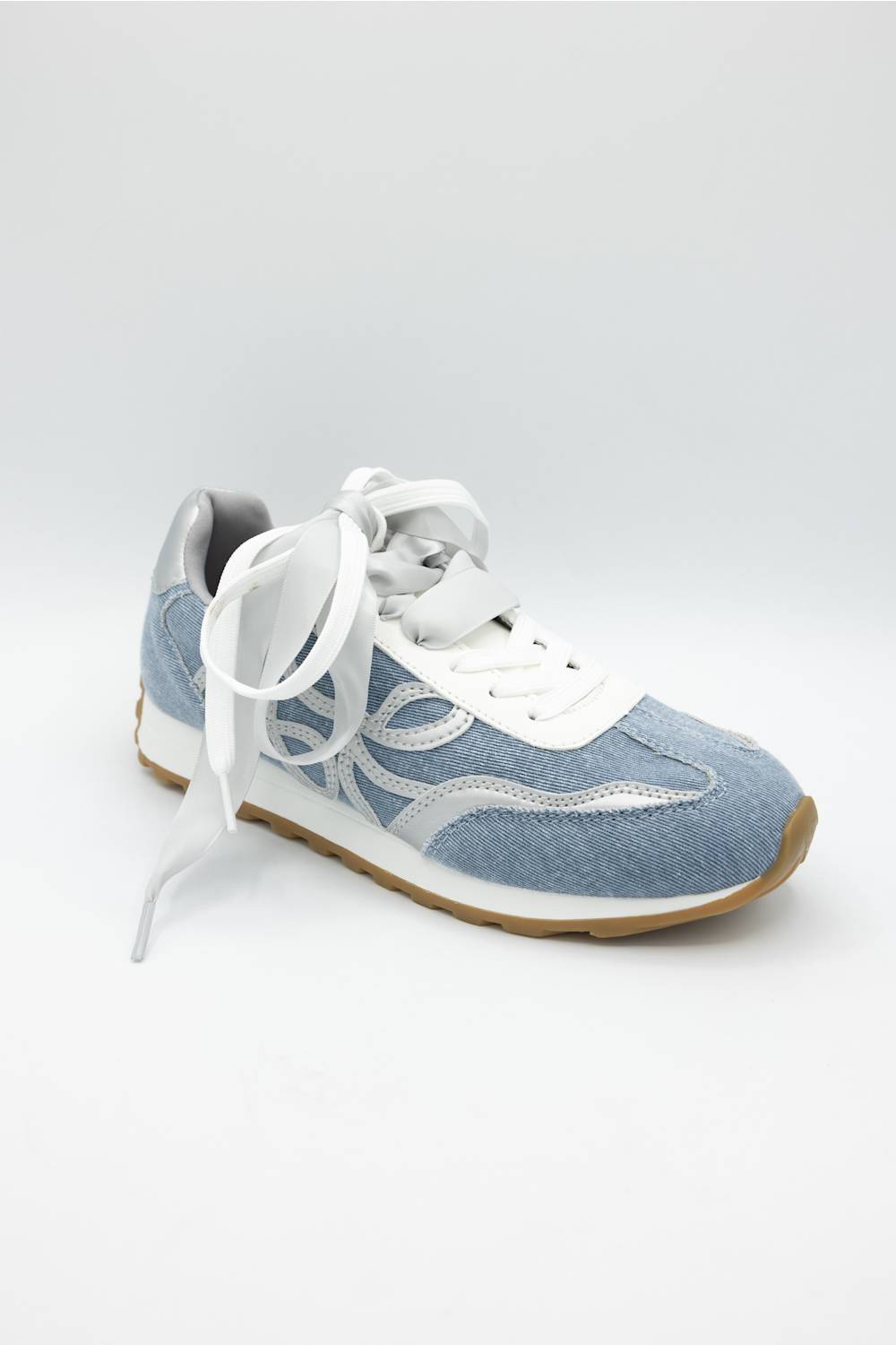A light blue and white low-top sneaker with white laces and a gum-colored outsole, photographed on a light gray studio background.
