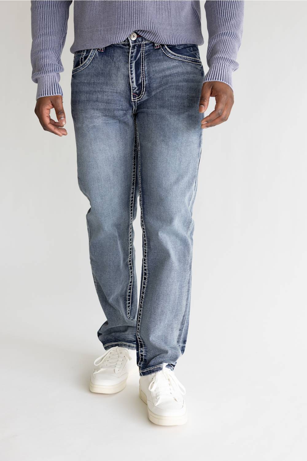 A person wearing light-wash blue jeans with a ribbed lavender sweater and white sneakers, shown from the waist down against a plain light background.