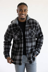 A man wearing a black and gray plaid hooded flannel shirt jacket over a black t-shirt and gray jeans, standing against a plain white background.