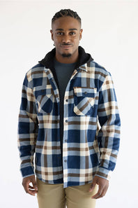 A man wearing a blue, beige, and brown plaid hooded flannel shirt over a dark gray t-shirt and khaki pants, standing against a plain white studio background.