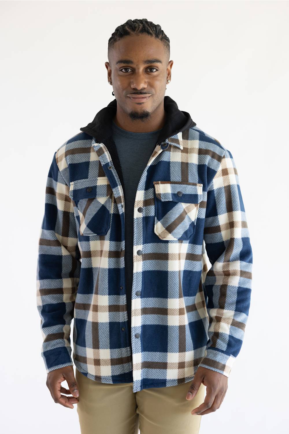 A man wearing a blue, beige, and brown plaid hooded flannel shirt over a dark gray t-shirt and khaki pants, standing against a plain white studio background.