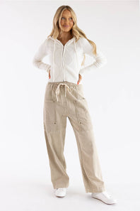 A woman modeling a white ribbed knit zip-up hoodie and beige wide-leg cargo pants with white sneakers, photographed against a seamless white studio background.