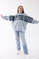 A woman modeling a light blue sweatshirt with 'SIMPLY FOR GOOD' written across the back in dark navy letters with white polka dots, paired with light blue jeans and white sneakers, against a plain white background.