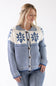 A woman wearing a blue and cream knit cardigan sweater with a button-front closure and Nordic snowflake patterns, paired with blue jeans against a plain white background.