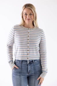 A woman modeling a light blue and beige striped button-up cardigan sweater with blue jeans, photographed against a plain white studio background.