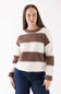 A woman wearing a brown and cream striped knit sweater with dark blue jeans, standing against a plain white studio background.