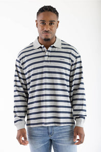 A man wearing a long-sleeve polo shirt with navy blue horizontal stripes on a light gray background, paired with blue jeans, photographed against a plain white studio background.