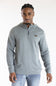 A man wearing a light gray ribbed quarter-zip hoodie with a small rectangular chest logo, paired with light blue jeans, photographed against a plain white studio background.