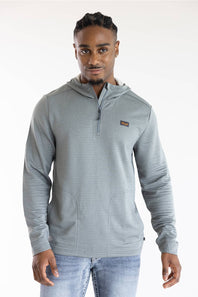 A man wearing a light gray ribbed quarter-zip hoodie with a small rectangular chest logo, paired with light blue jeans, photographed against a plain white studio background.