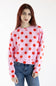A woman with red hair wearing a pink long-sleeve sweatshirt with large red polka dots, paired with blue jeans, against a plain white background.