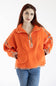 A woman wearing an oversized bright orange fleece pullover with floral patterned trim on the collar, zipper placket, cuffs, and hem, paired with blue jeans, against a plain white background.