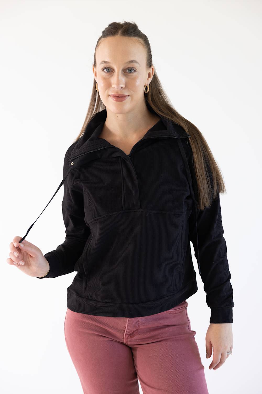 A woman modeling a black long-sleeve quarter-zip pullover sweatshirt with a mock neck, paired with dusty rose pants, against a plain white studio background.