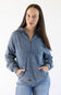 A woman modeling a washed blue half-zip hoodie with a drawstring hood and front kangaroo pockets, paired with blue jeans, against a plain white studio background.