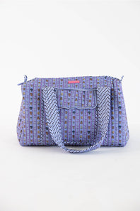 A purple patterned tote bag with a front pocket, braided shoulder strap, and small pink brand tab, photographed on a clean white background.