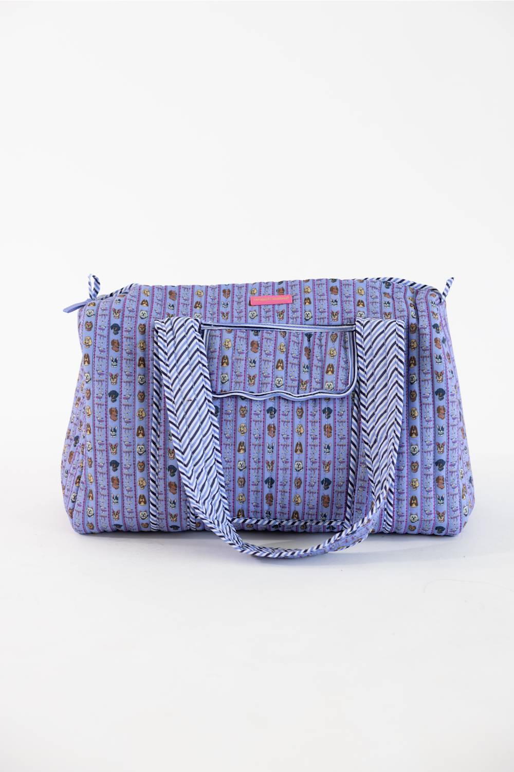 A purple patterned tote bag with a front pocket, braided shoulder strap, and small pink brand tab, photographed on a clean white background.
