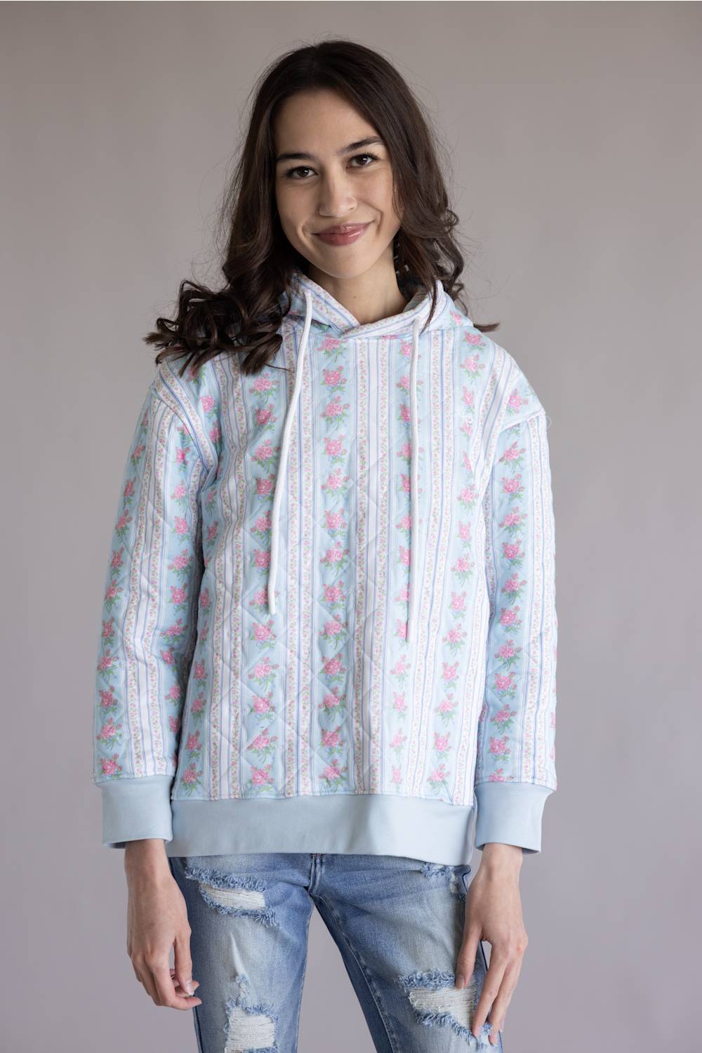 Simply Southern Quilted Hoodie for Women in Rose Stripe; Woman wearing a light blue hoodie with floral patterns against a plain background