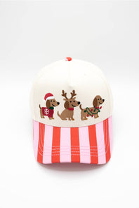 Front view of the Simply Southern Santa Dogs Holiday Hat in Cream/Stripe against a white background, featuring three embroidered dachshunds dressed in Christmas outfits on the cream front panel and a vertical red and pink striped visor.