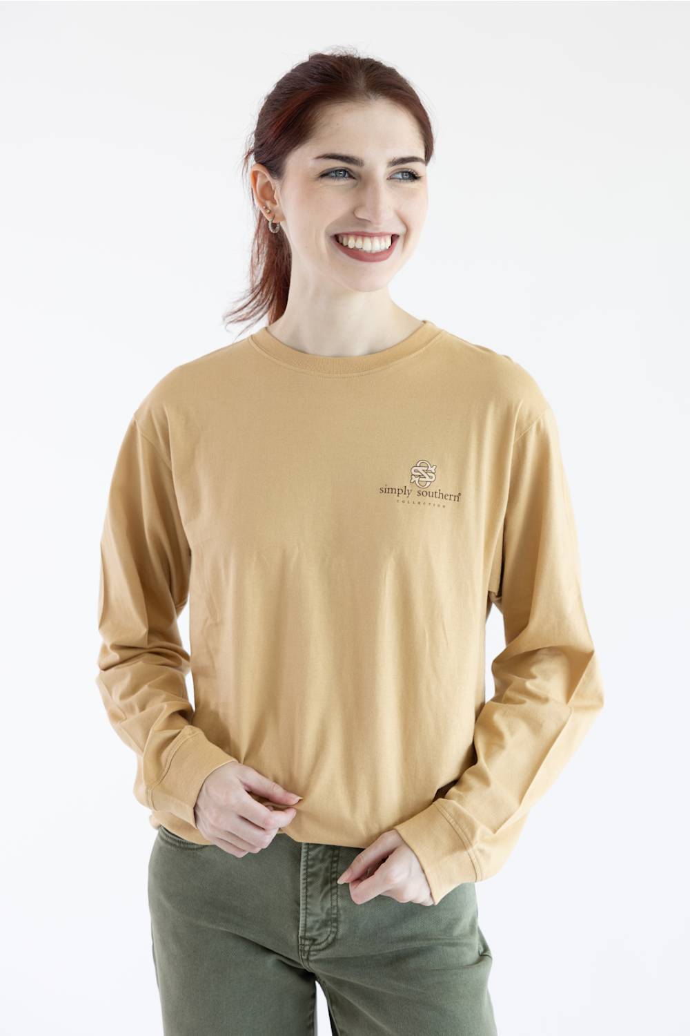A woman wearing a tan long-sleeve crewneck shirt with a small embroidered 'simply southern' logo on the left chest, set against a plain white background.