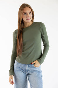 A woman modeling a long-sleeve crewneck top in olive green, paired with light-wash blue jeans, against a plain white studio background.