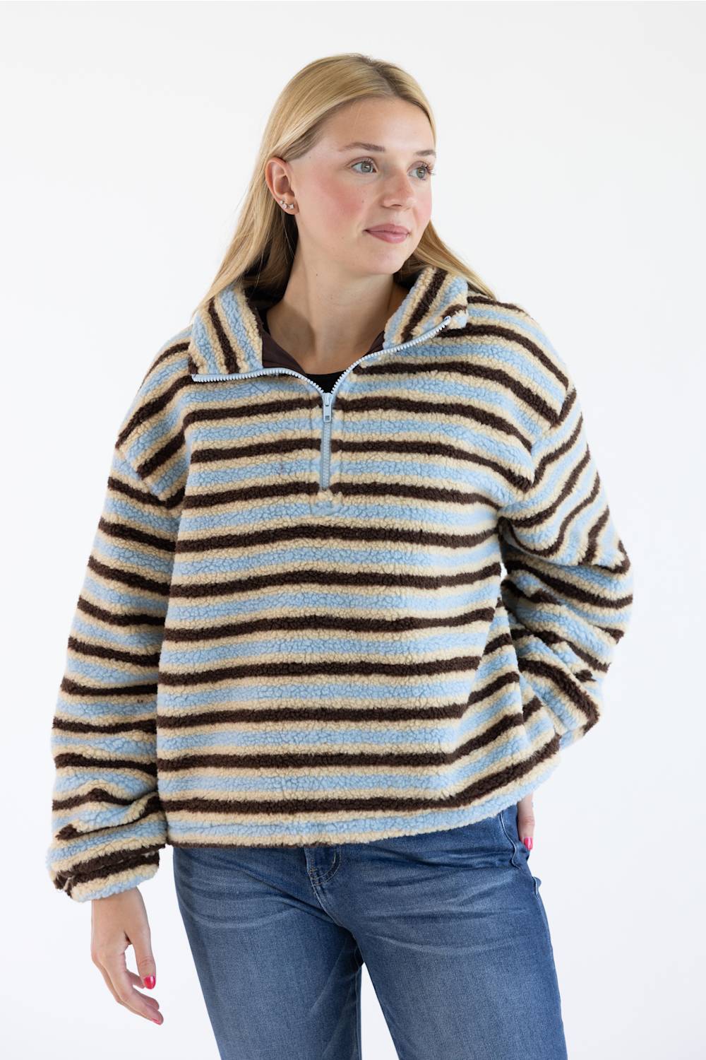 A woman wearing a fuzzy quarter-zip pullover sweater with horizontal stripes in light blue, cream, and dark brown, paired with blue jeans, against a plain white background.