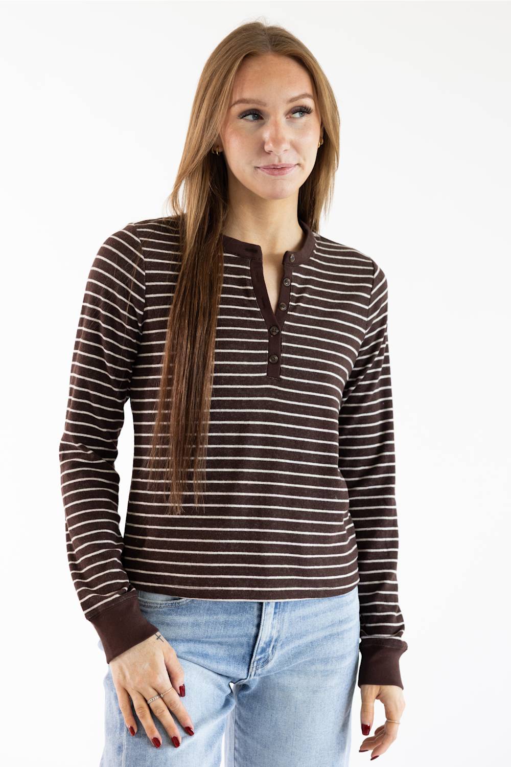 A woman modeling a brown and white horizontally striped long-sleeve henley shirt with light blue jeans, set against a plain white studio background.