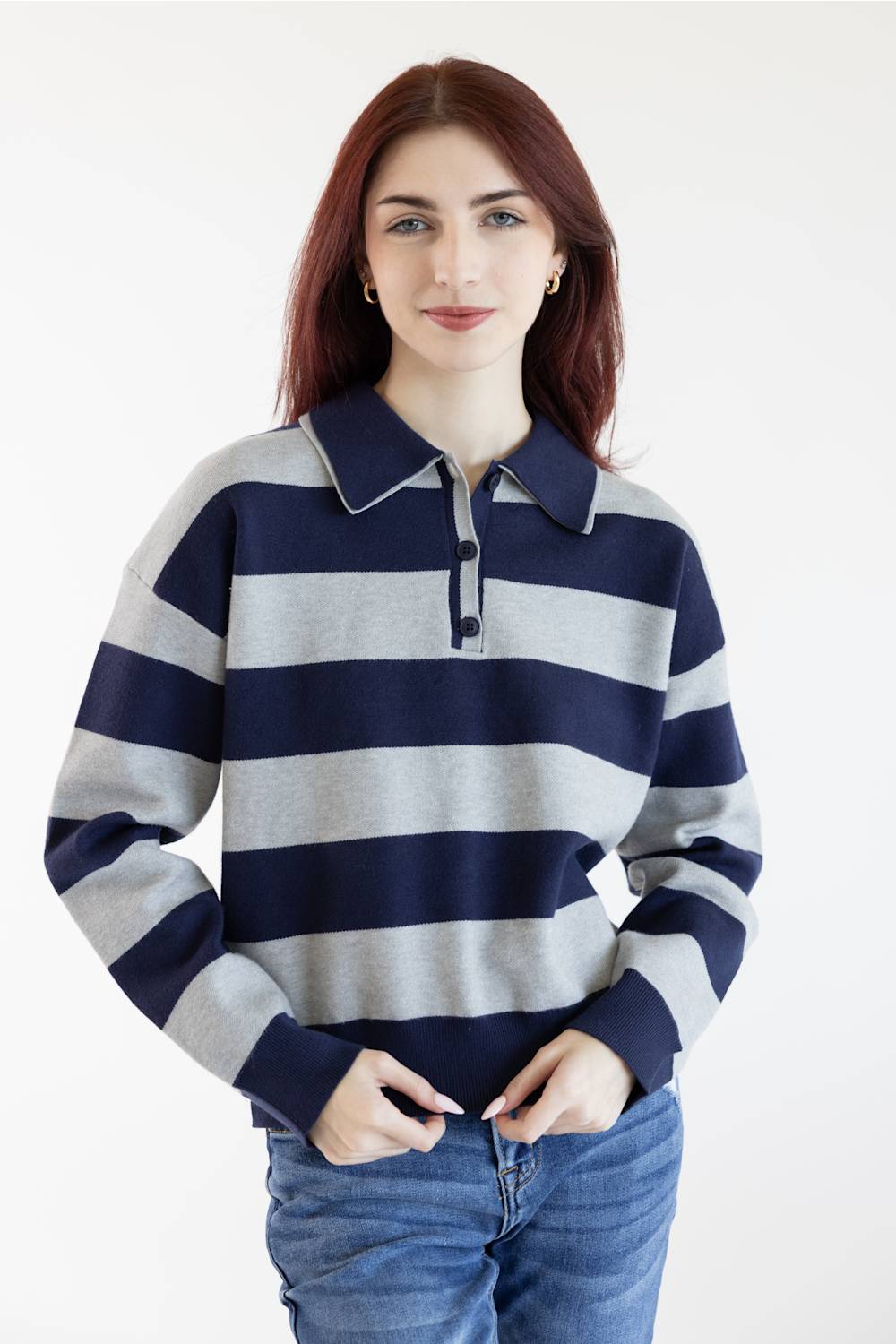 A woman with red hair wearing a navy and gray horizontally striped long-sleeve polo sweater and blue jeans, standing against a plain white background.