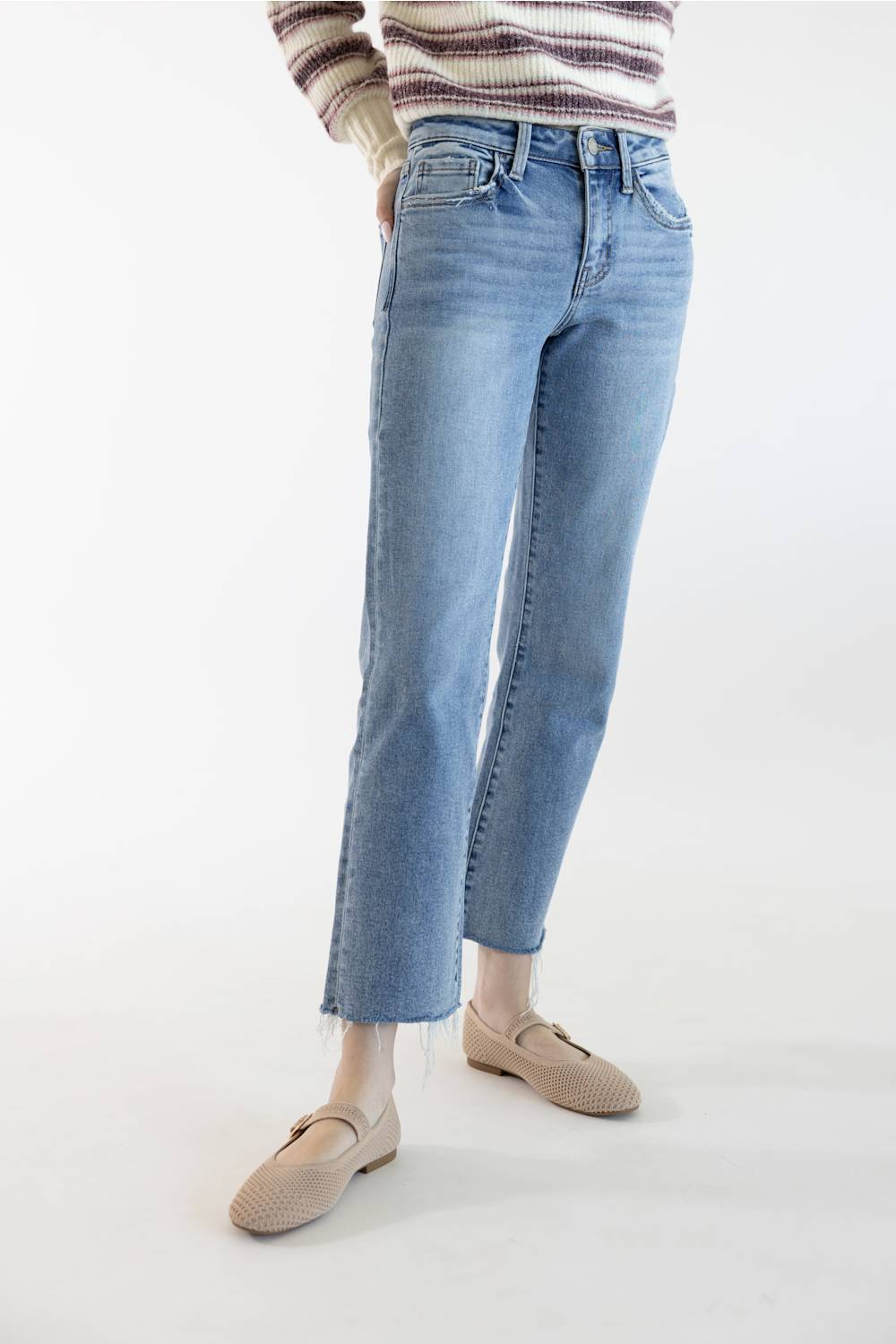 A person wearing light-wash blue cropped jeans with a striped knit top and beige loafers, standing against a plain white studio background.