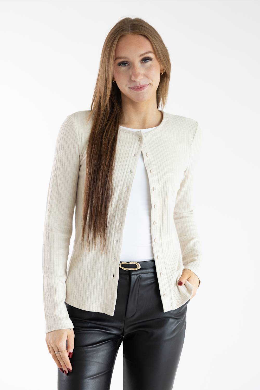 A woman modeling a cream ribbed knit cardigan over a white top and black faux-leather pants, photographed against a plain white studio background.
