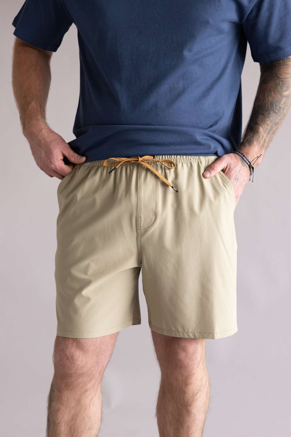 Person wearing a navy shirt and beige shorts on a plain background. The beige shorts are the Quiksilver Taxer Amphibian 18" Hybrid Shorts for Men in Twill 