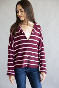 A woman wearing a burgundy and light pink striped knit cardigan with a collar and button front, paired with a white top and blue jeans, photographed against a plain light gray background.
