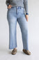 A person wearing light-wash blue straight-leg jeans, a navy and white striped long-sleeve top, and brown suede loafers, standing against a plain light gray studio background.