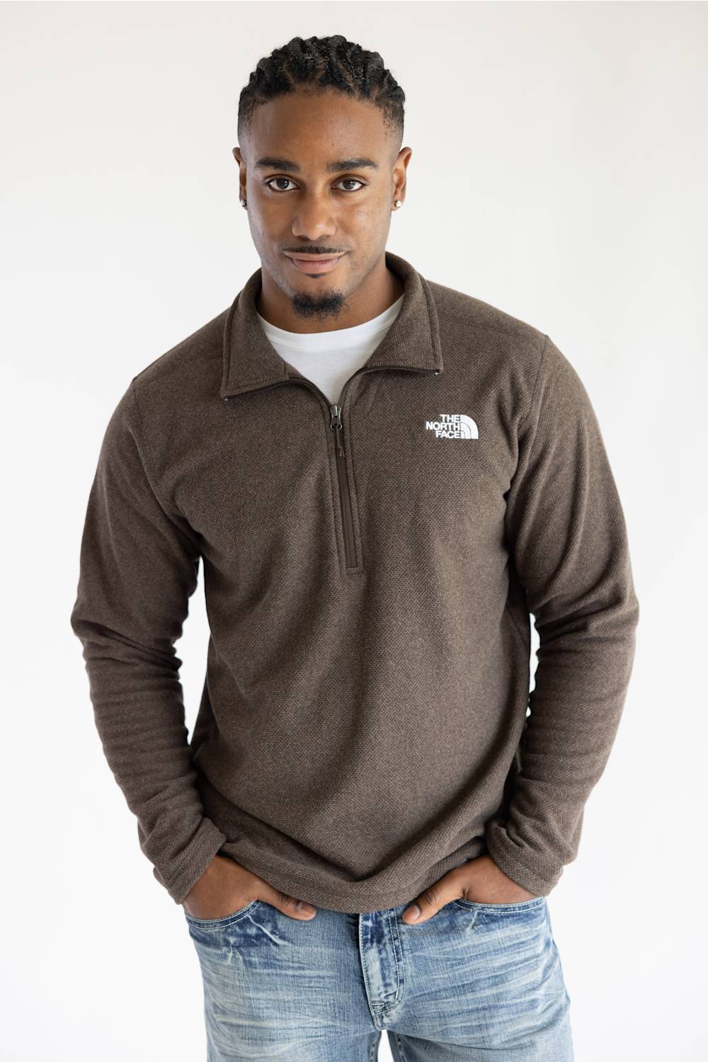 A man wearing a brown quarter-zip fleece pullover by The North Face, styled over a white t-shirt and blue jeans, standing against a plain white background.