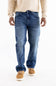 A person wearing medium-wash blue jeans, a cream long-sleeve shirt, and tan suede shoes, shown from the chest down against a plain white studio background.