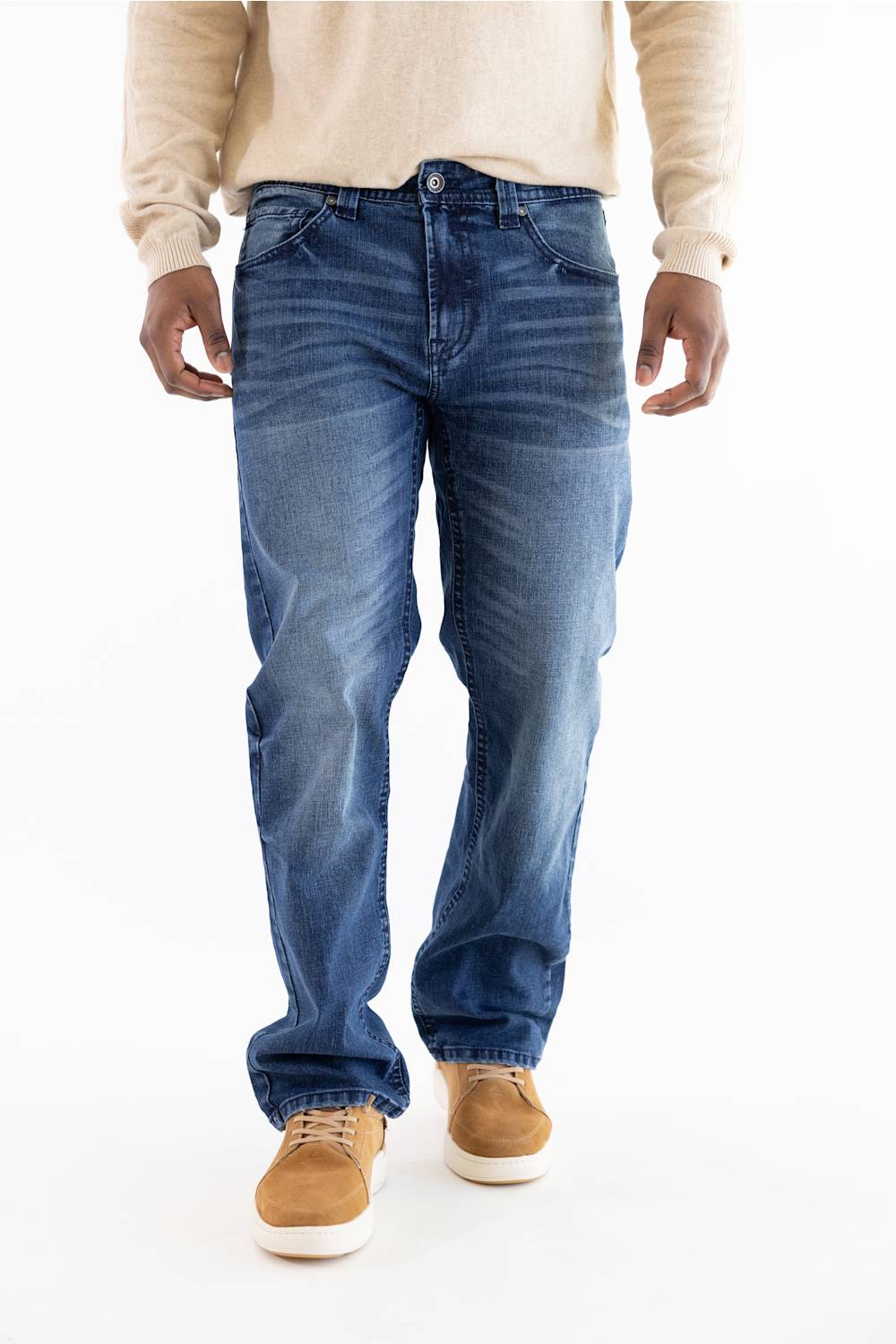 A person wearing medium-wash blue jeans, a cream long-sleeve shirt, and tan suede shoes, shown from the chest down against a plain white studio background.