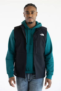 A person wearing a black vest over a teal hoodie, with The North Face logo printed in white on the upper chest.