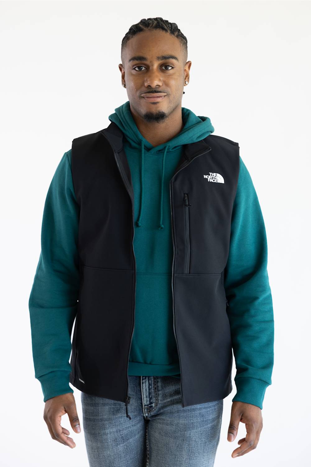 A person wearing a black vest over a teal hoodie, with The North Face logo printed in white on the upper chest.