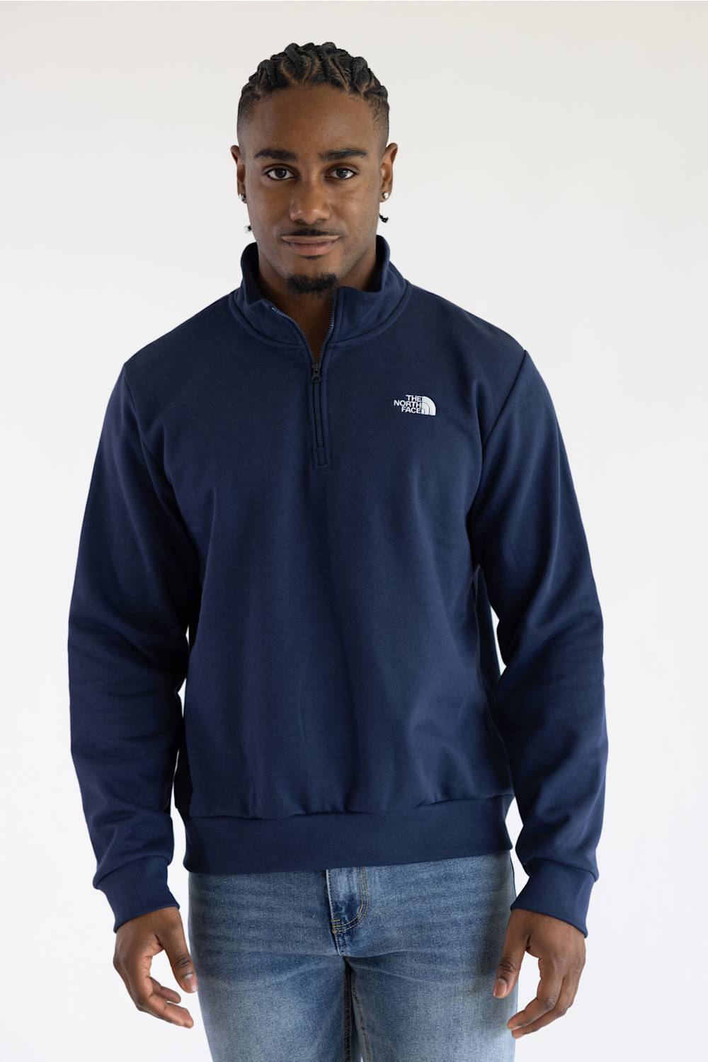 A man wearing a navy long-sleeve quarter-zip pullover jacket and blue jeans, set against a plain white studio background.