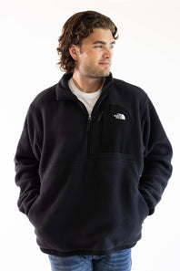 A man wearing a black fleece quarter-zip pullover by The North Face, styled over a white t-shirt and blue jeans, photographed against a plain white background.