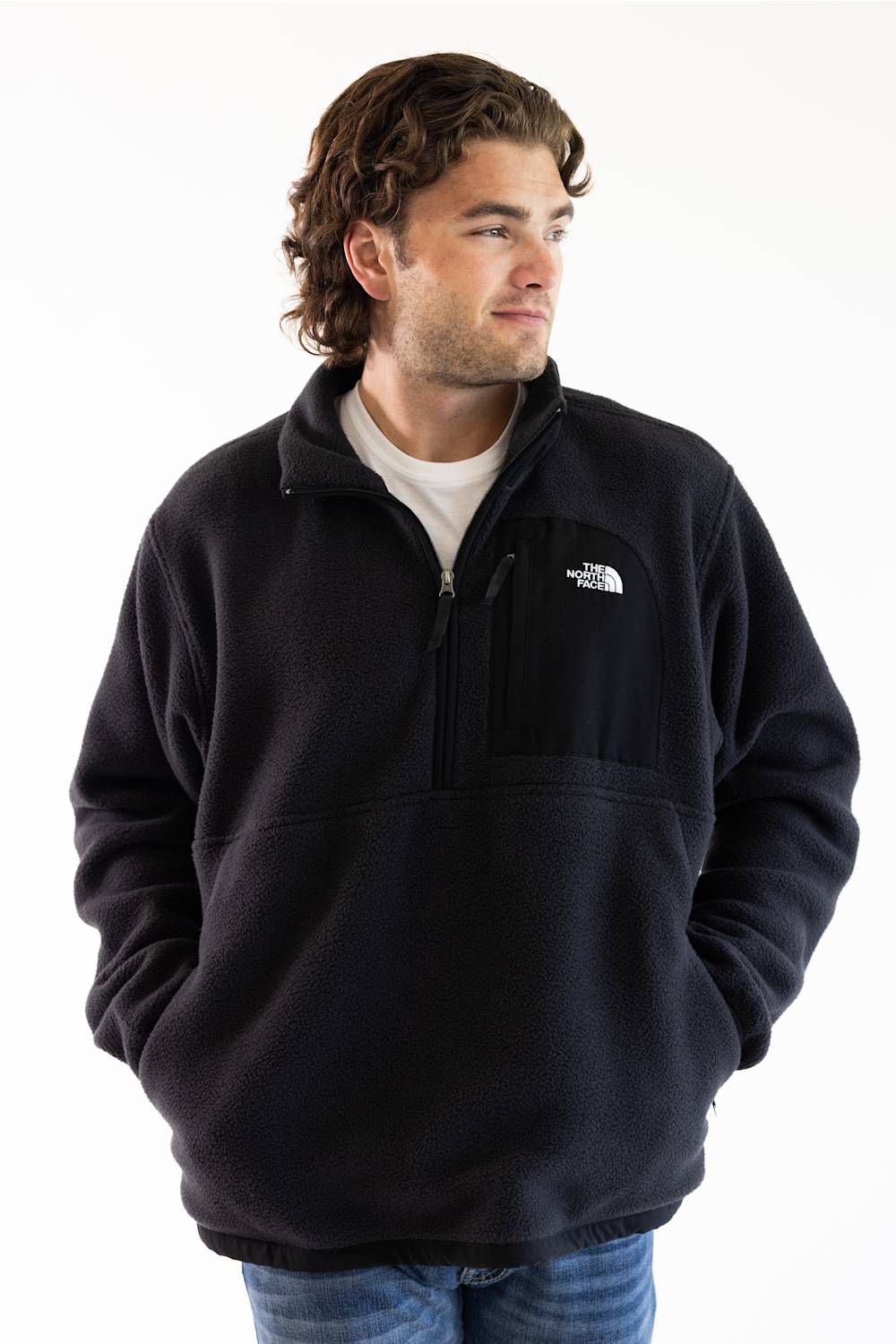 A man wearing a black fleece quarter-zip pullover by The North Face, styled over a white t-shirt and blue jeans, photographed against a plain white background.