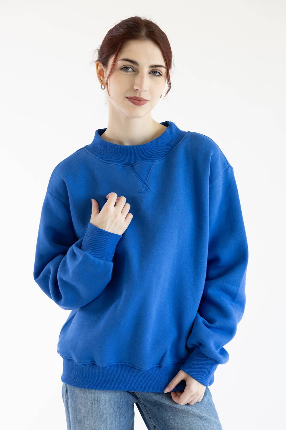 A woman wearing a vibrant royal blue crewneck sweatshirt and light wash jeans, standing against a plain white studio background.