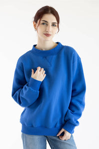 A woman wearing a vibrant royal blue crewneck sweatshirt and light wash jeans, standing against a plain white studio background.