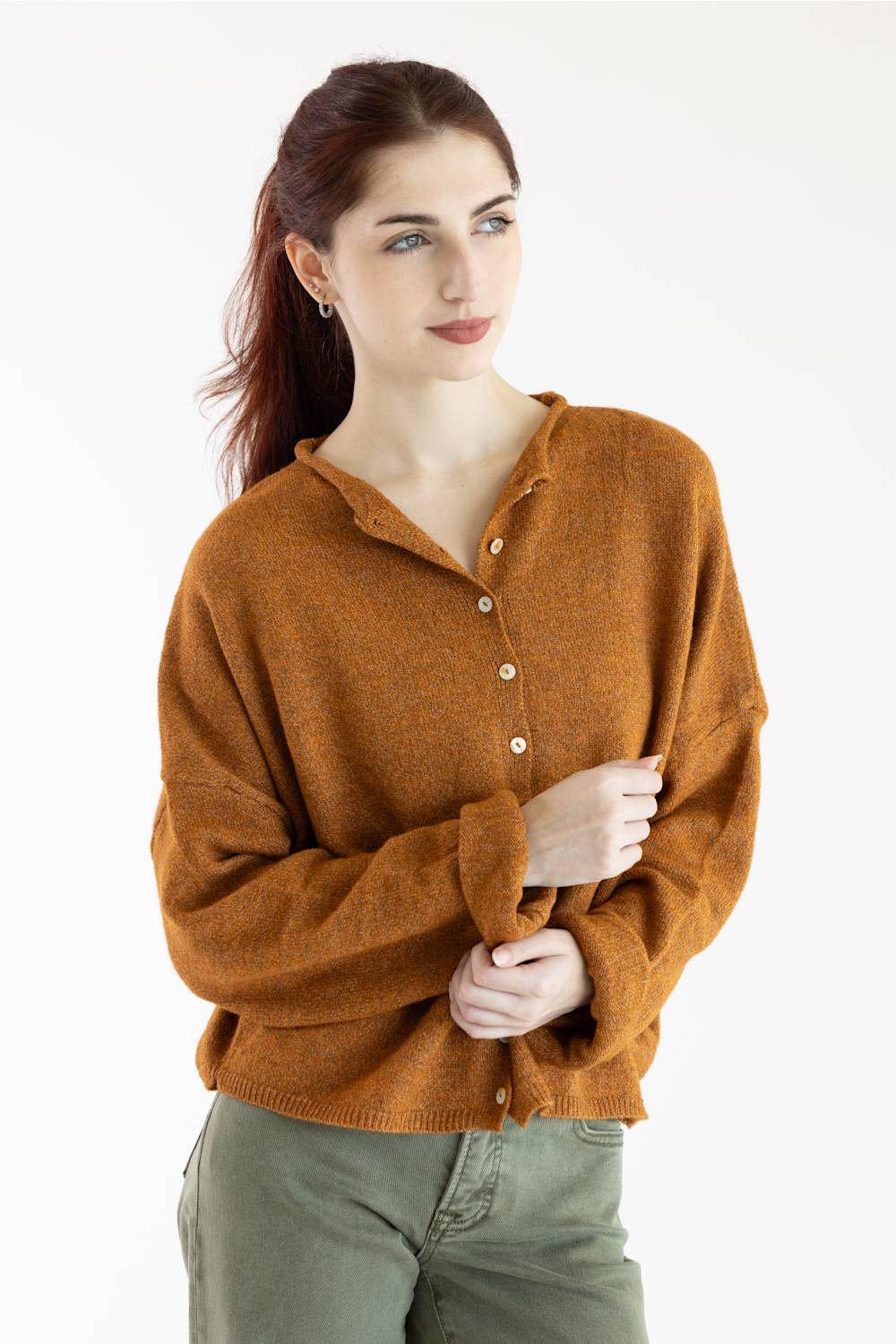 A woman wearing a warm rust-orange knit button-front cardigan sweater with a split neckline, paired with olive green pants, photographed against a clean white studio background.
