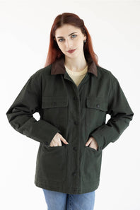 A woman with red hair wearing an oversized dark olive green utility jacket with a brown collar, over a cream sweater and blue jeans, photographed against a plain white background.