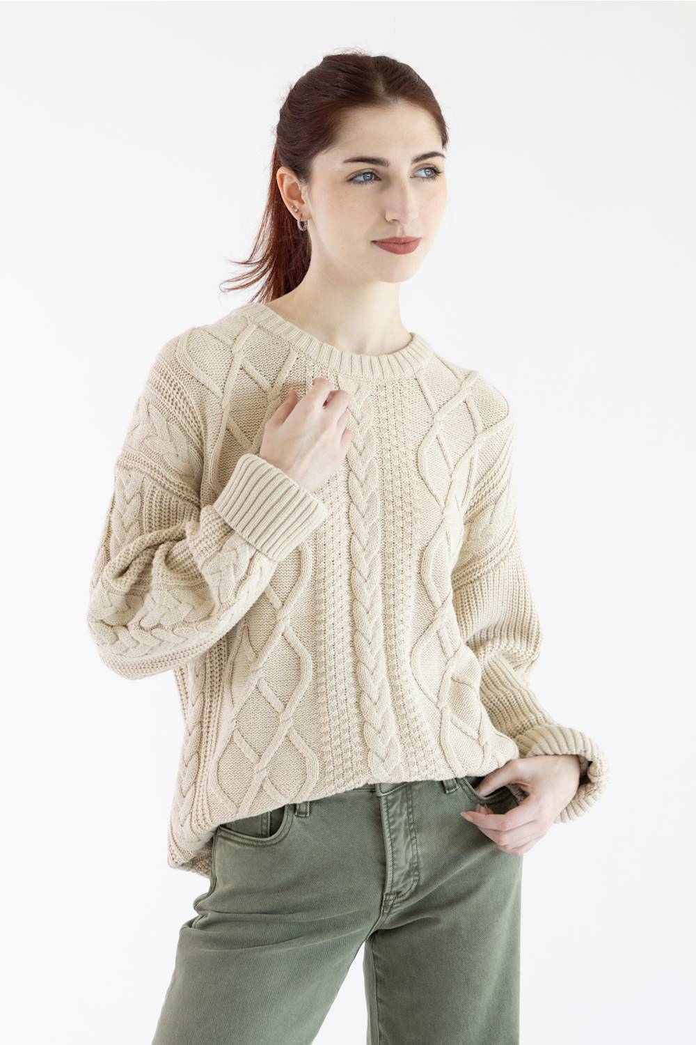 A woman wearing a cream-colored cable-knit sweater and olive green pants, shown from the neck down against a plain white background.