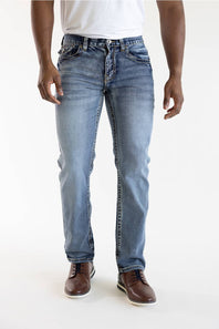 A person wearing light blue slim-fit jeans with a white t-shirt and brown leather shoes, shown from the waist down against a plain white studio background.