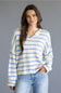 A woman wearing a cream-colored knit cardigan with thin blue horizontal stripes, paired with light-wash blue jeans, against a solid gray studio background.
