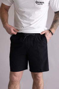 Person wearing a white t-shirt with a logo and black shorts on a plain background. The shorts are the Quiksilver Union Amphibian 20" Hybrid Shorts for Men in Black.