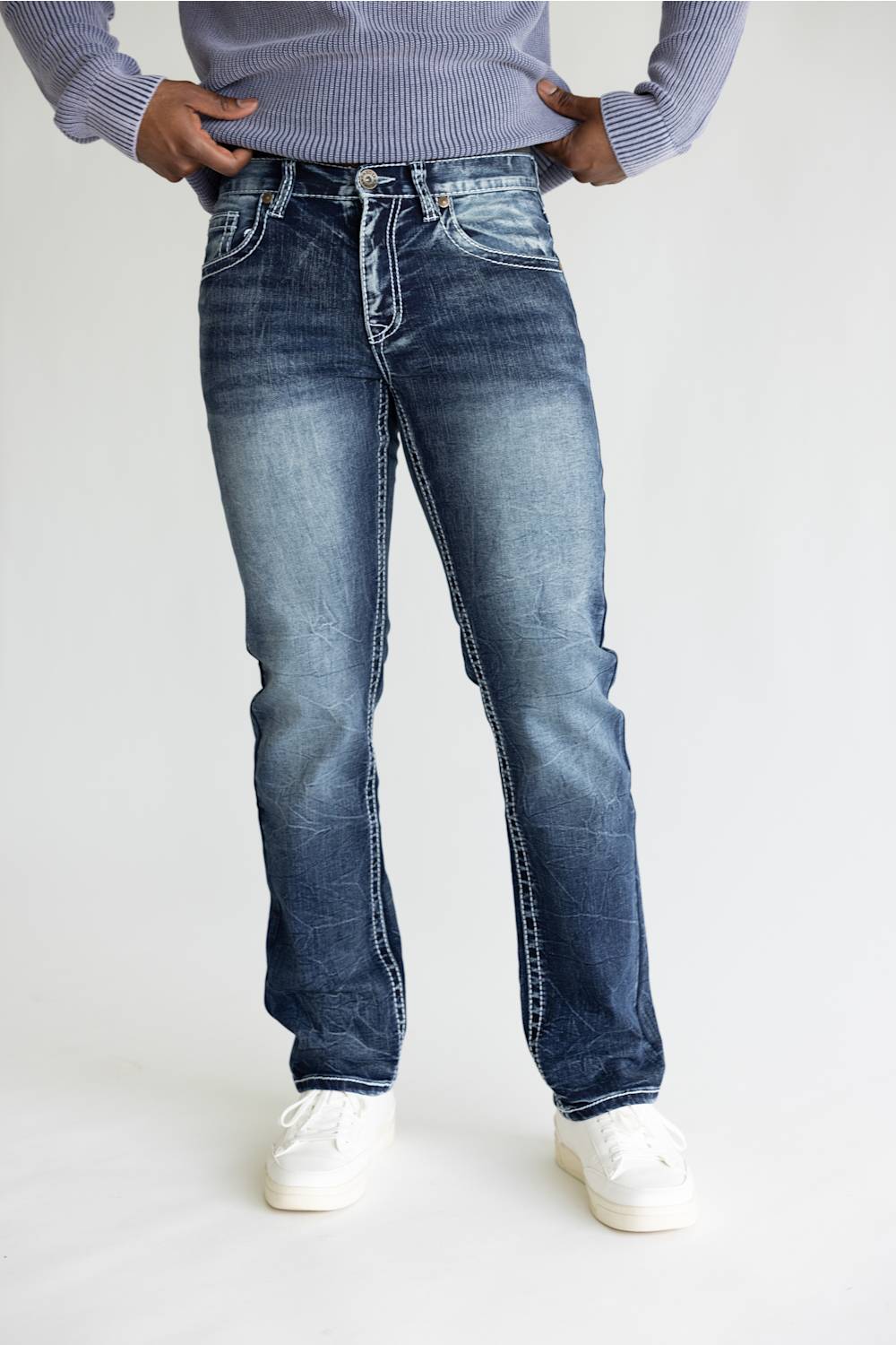 A person wearing blue denim jeans with a faded wash, paired with a light purple ribbed sweater and white sneakers, shown from the waist down against a plain light background.